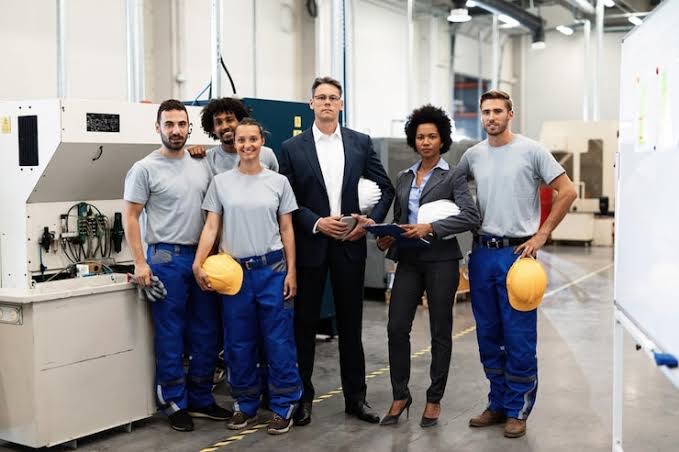 The full team standing together in the shop in front of the equipment, hard hats in hand.