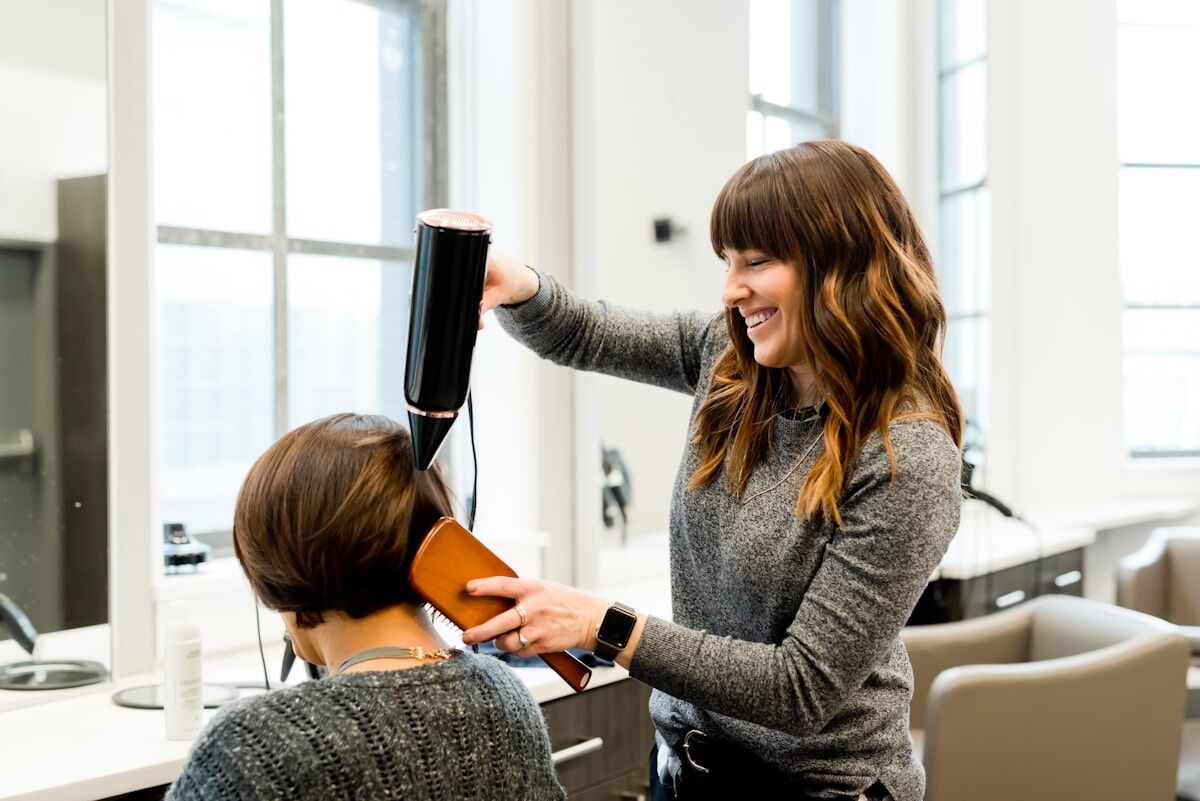 A stylist laughing with a client while finishing a blowout